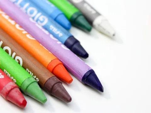 Poza cu mai multe creioane colorate de culori diferite asejate unul langa altul pe o masa de culoare alba