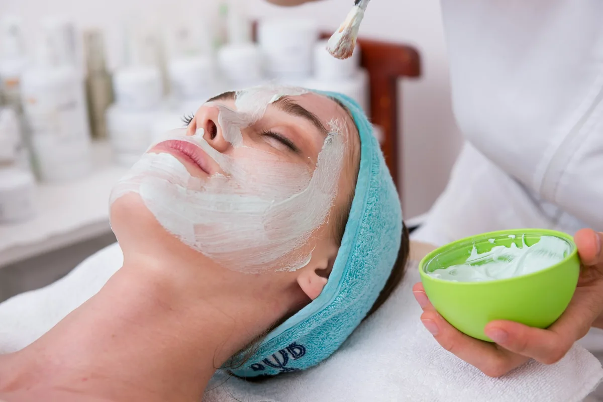 Masca pentru ingrijirea tenului aplicat pe fata unei femei de catre o cosmeticiana