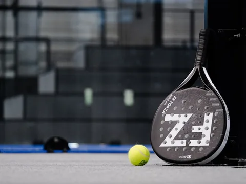 Poza in care se vede o paleta de Padel si o minge de Padel intr-o sala amenajata special pentru practicarea sportului de Padel Tenis