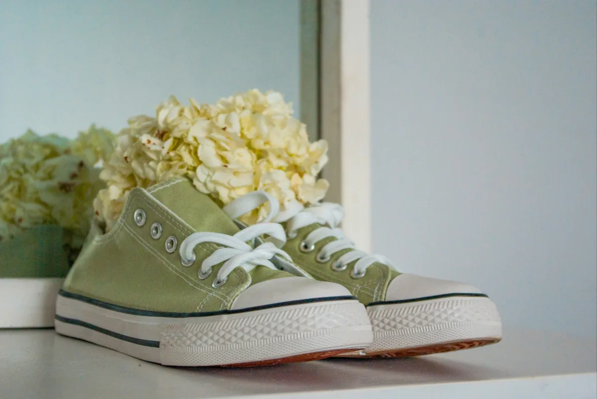 Poza cu o pereche de tenisi verde deschis cu un buchet de flori mici albe in interiorul lor care se refera la incaltamintea de vara