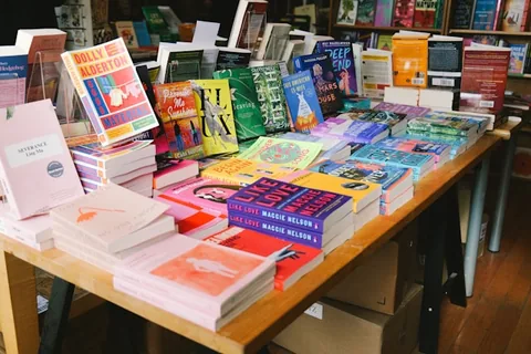 Poze cu mai multe carti pentru citit asezate pe o masa intr-o biblioteca unde sunt puse la vanzare