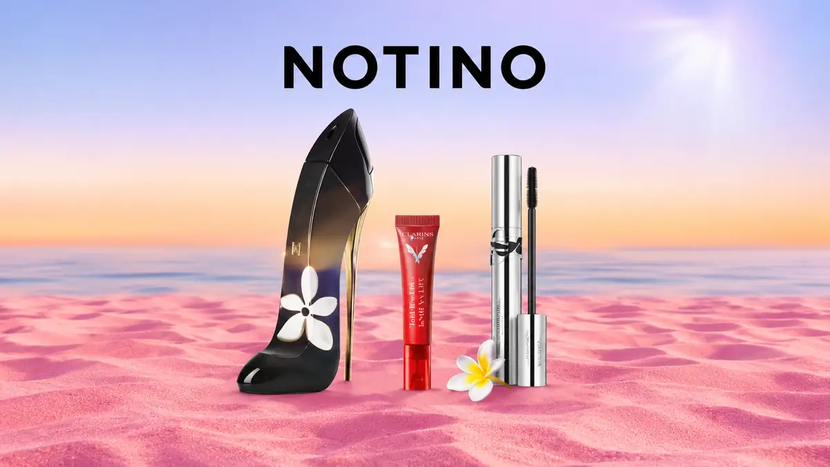 Produse cosmetice și parfum Notino pe nisip roz, cu fundal de mare la apus și logo Notino deasupra.